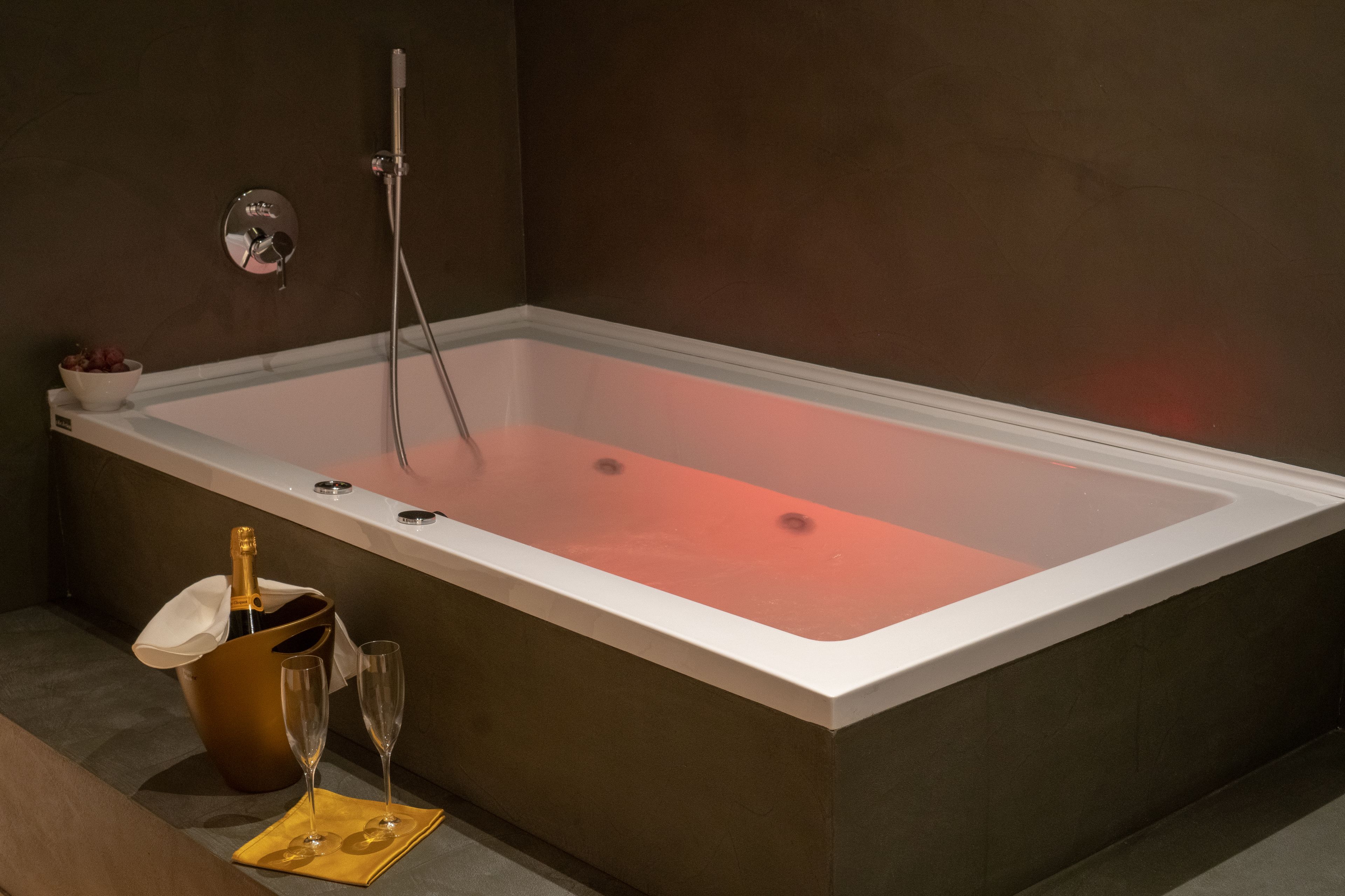 Een moderne badkamer met een rechthoekig bad, een handdouche en een fles champagne.