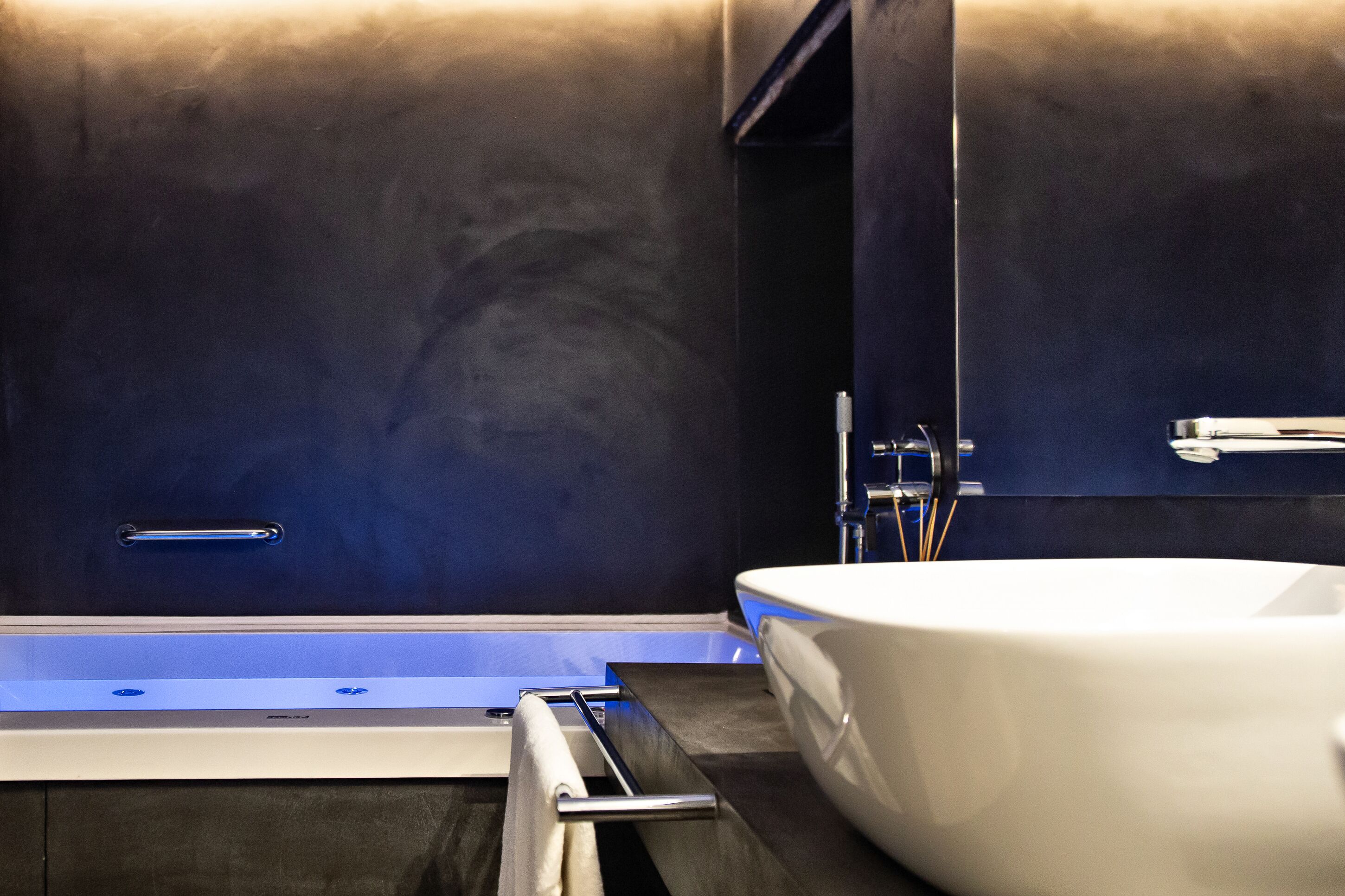 Un bagno moderno con una vasca da bagno ampia, un lavandino bianco e una parete scura.