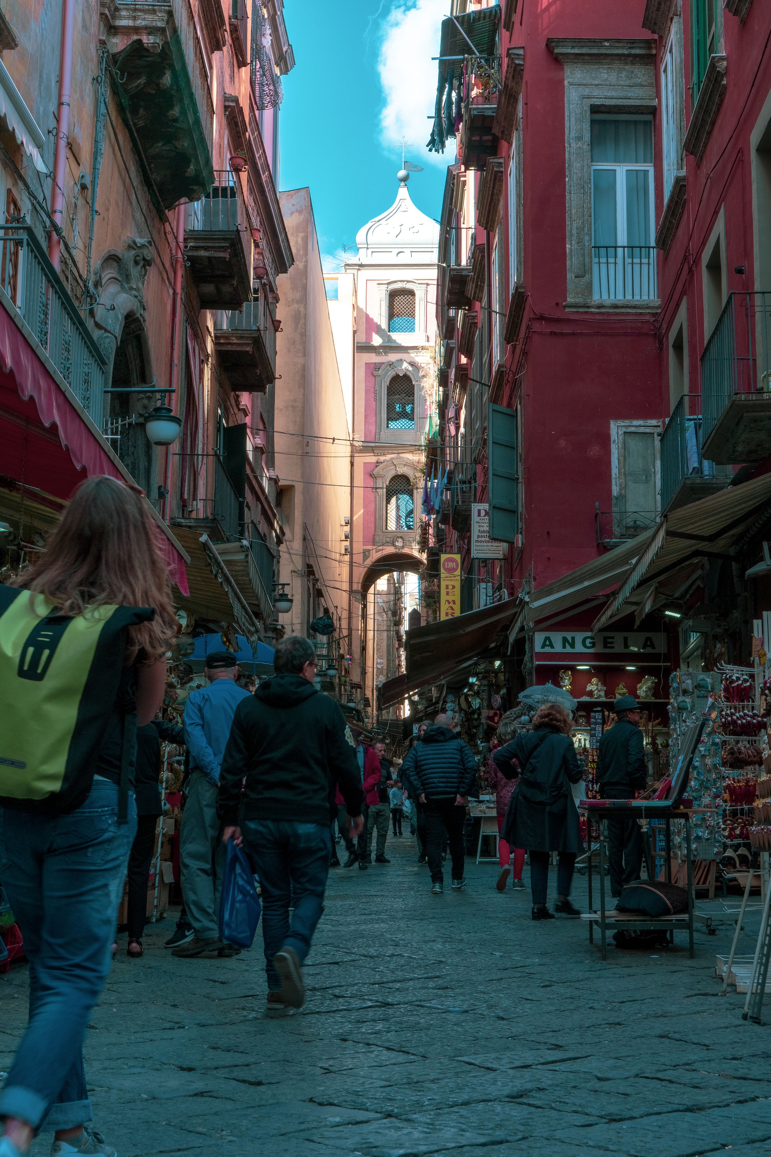 A narrow street with buildings on either side, a church with a dome, and people walking.