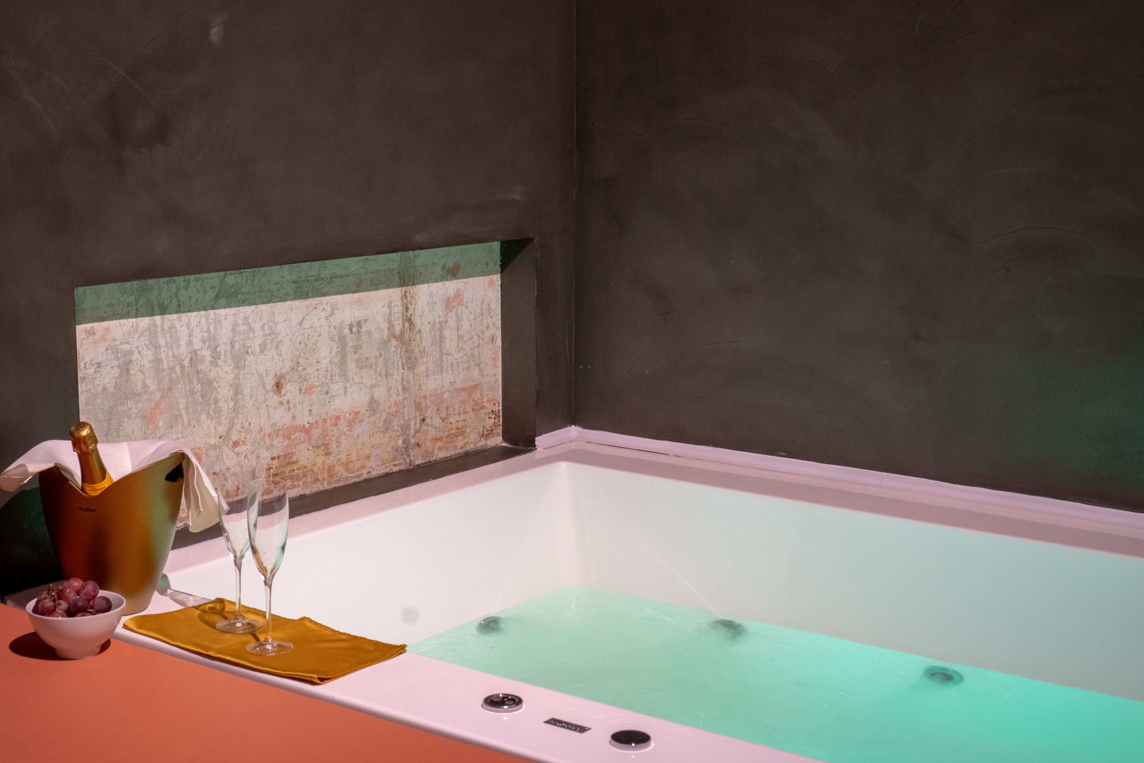 Una vasca da bagno con una sfumatura verdognola, un secchio di champagne e due bicchieri da champagne su un tavolo.