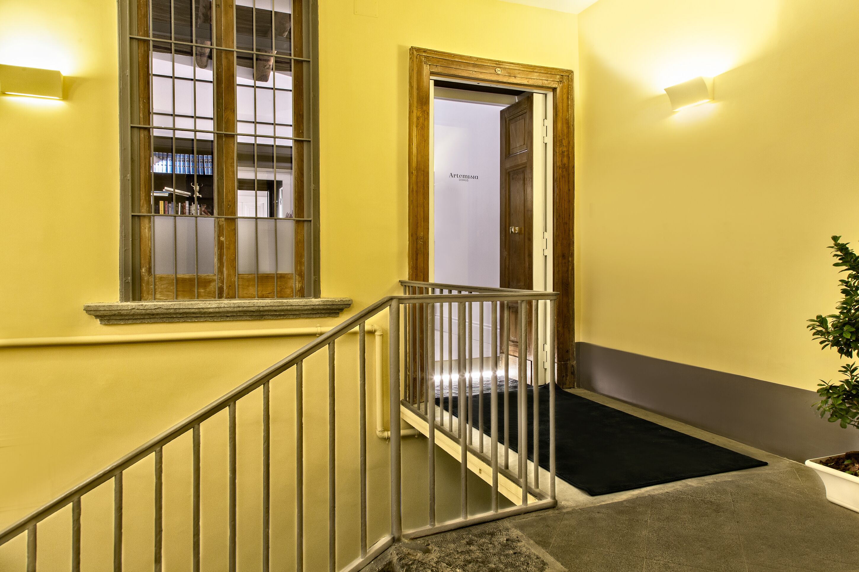 A staircase with a metal railing, a wooden door, and a black mat at the bottom.