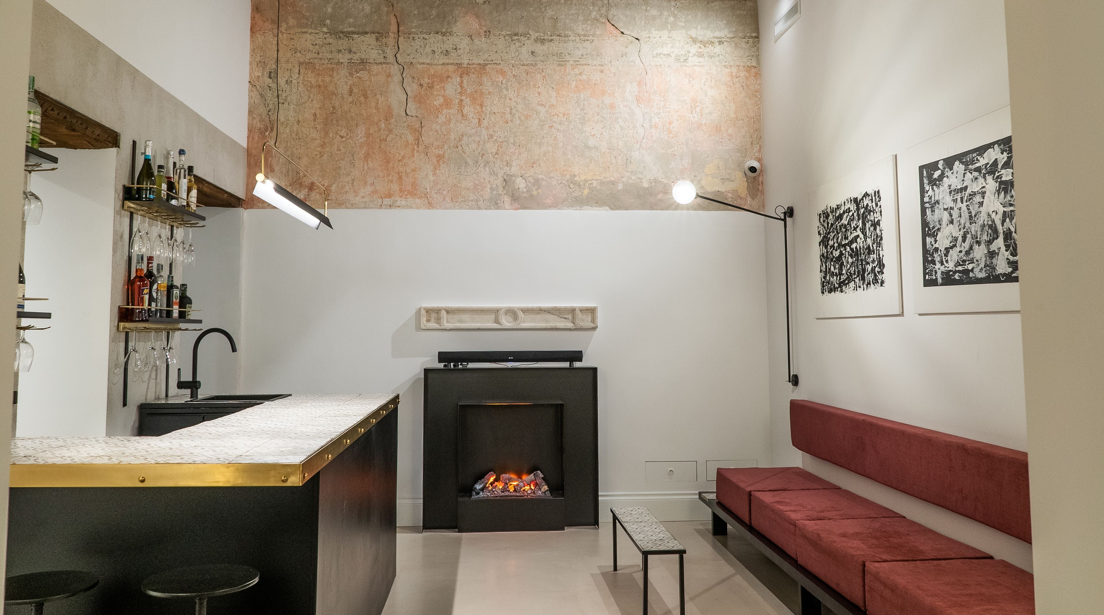 A modern living room with a fireplace, a red sofa, a kitchen area with a bar, and artwork on the walls.