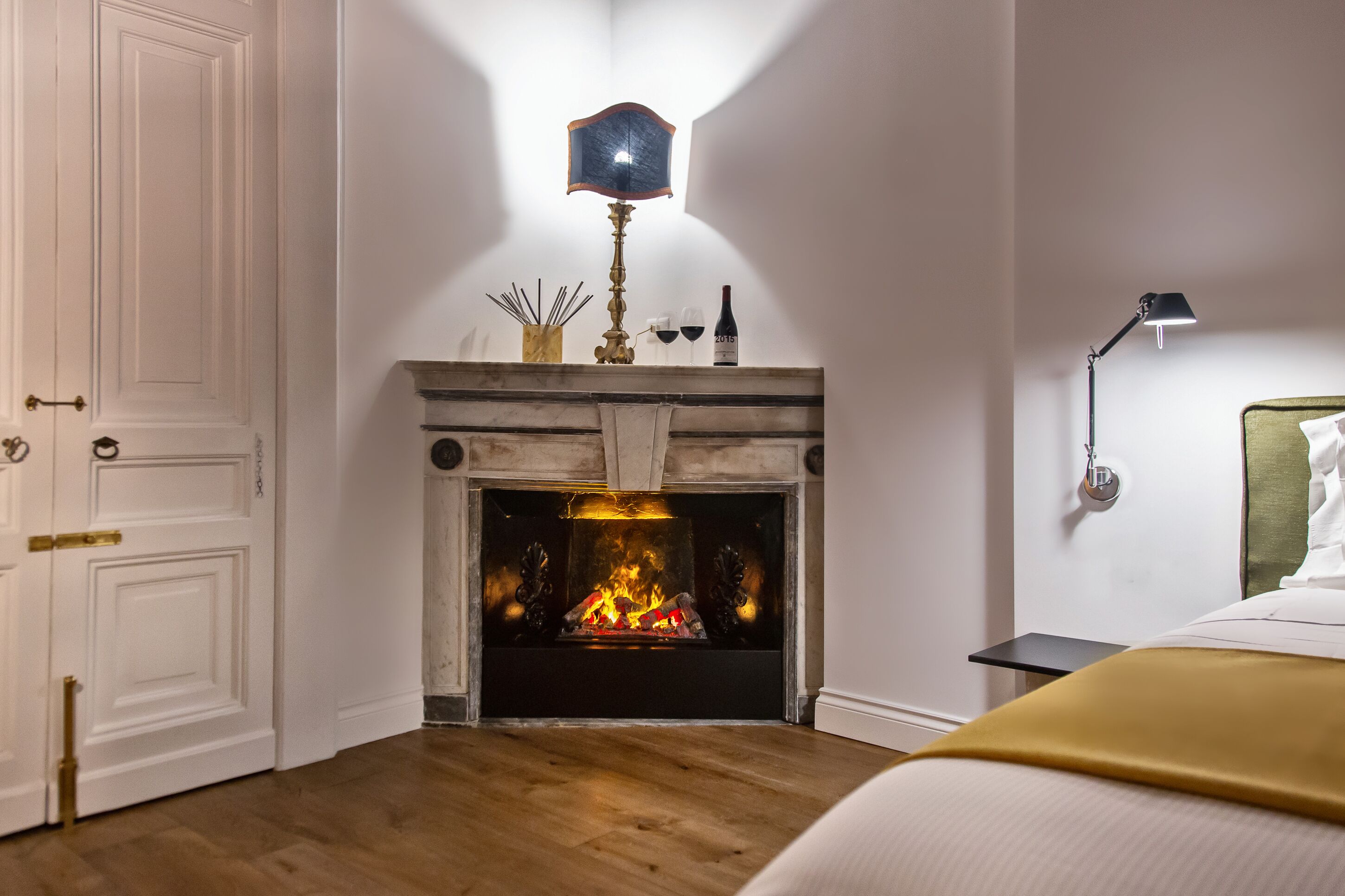 Una habitación con chimenea, una cama, una mesita de noche y una lámpara de pared.
