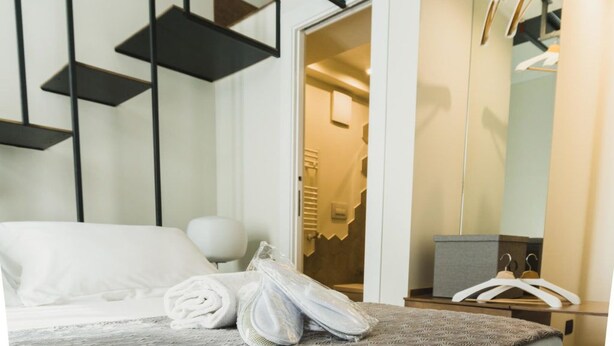A neatly made bed with rolled towels, a bedside table, a mirror, and a wardrobe with a hanging rack. - Catania House (Catania)