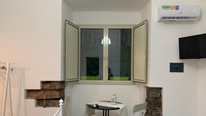 A corner room with a table and two chairs, a window with open shutters, a mounted air conditioner, and a flat-screen TV on the wall. - Catania House (Catania)
