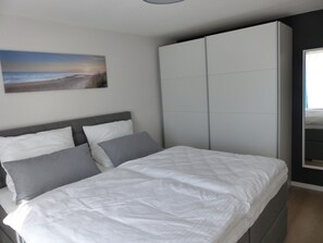 A bedroom with a bed, grey and white pillows, a large wardrobe, and a painting of a beach scene on the wall. - Ferienwohnungen Flora (Bad Windsheim)