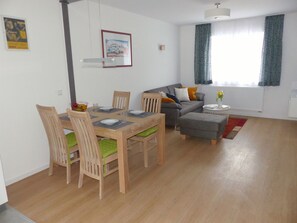 A modern living room with a dining area, featuring a sofa, a coffee table, and a dining table set for four. - Ferienwohnungen Flora (Bad Windsheim)