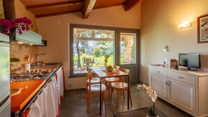 A kitchen with a dining table and chairs, a TV, and a window with blinds. - Agriturismo Torribasse (Magliano in Toscana)