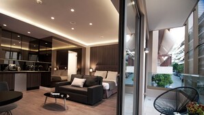A modern living room with a sofa, coffee table, and a dining area. There is a kitchen area with a dishwasher and a large mirror. The room has a balcony with a view of the street and greenery. - Athens Platinum Rooms and Suites (Athens)