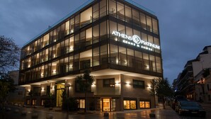 A modern hotel with a glass facade, named "Athens Platinum," featuring multiple floors and a well-lit entrance. - Athens Platinum Rooms and Suites (Athens)