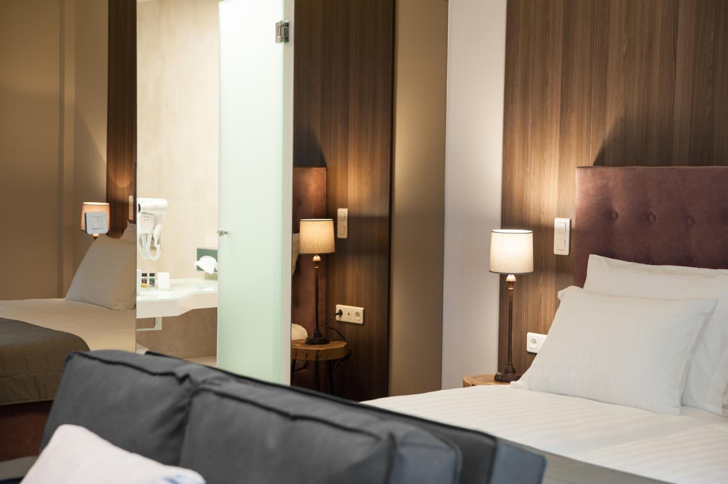 A hotel room with a bed, a bedside table with a lamp, a mirror, and a wall-mounted light fixture.