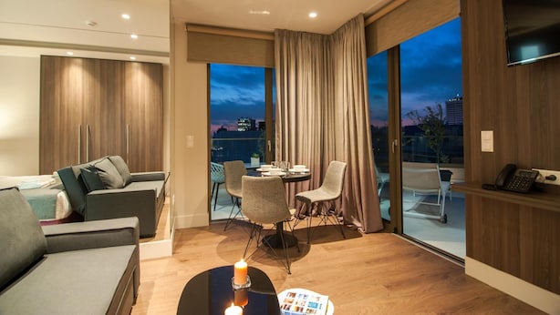A modern living room with a sofa, dining table, and chairs, a fireplace, and a view of the cityscape through large windows. - Athens Platinum Rooms and Suites (Athens)