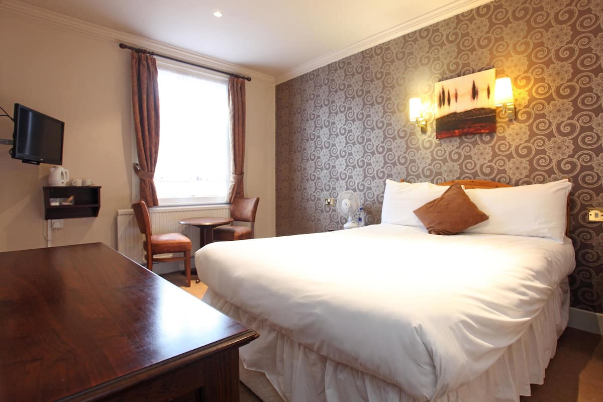 A hotel room with a large bed, a wooden desk, a chair, a television, and a window with curtains.