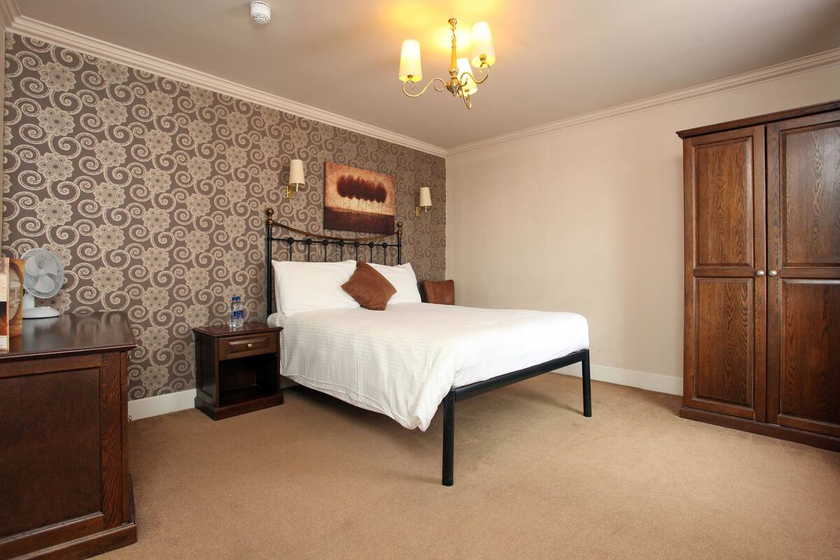 A bedroom with a bed, nightstands, a wooden wardrobe, and a patterned wallpaper.