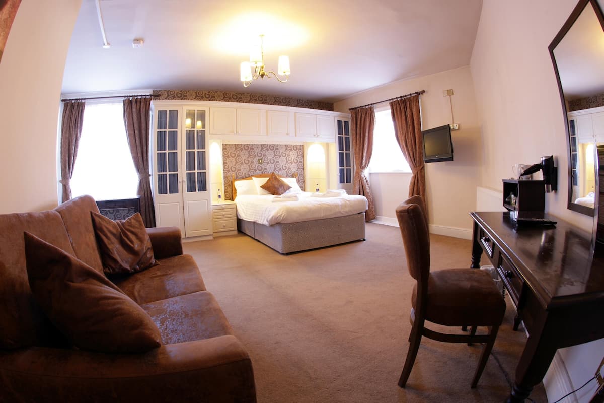 A hotel room with a large bed, a sofa, a desk, and a TV.