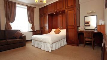 Ein Hotelzimmer mit einem großen Bett, einem Schreibtisch und einem Stuhl. Es gibt ein Fenster mit Vorhängen, eine Chandelier und einen Spiegel an der Wand.