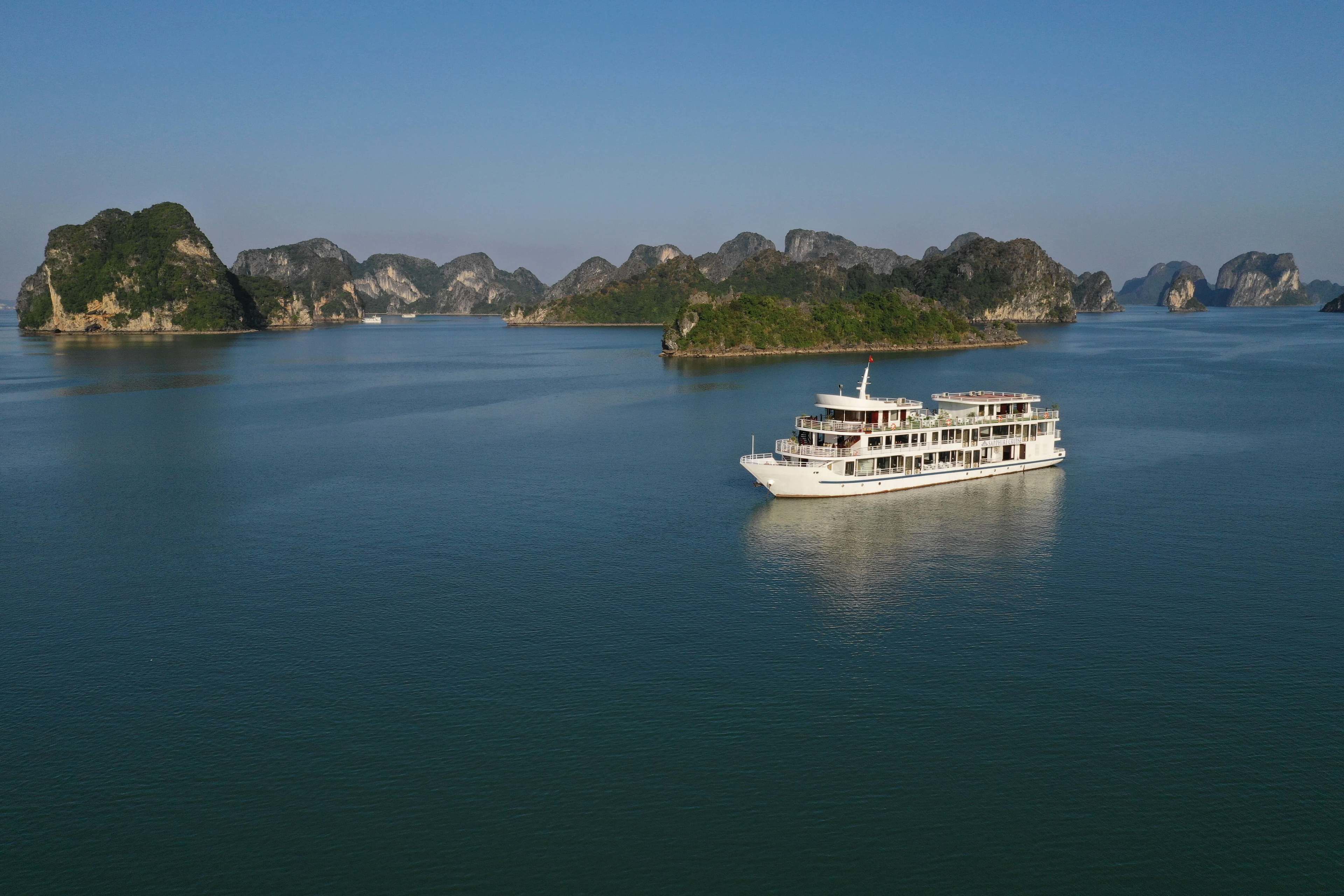 A large white boat with multiple decks on calm water, surrounded by rocky islands.