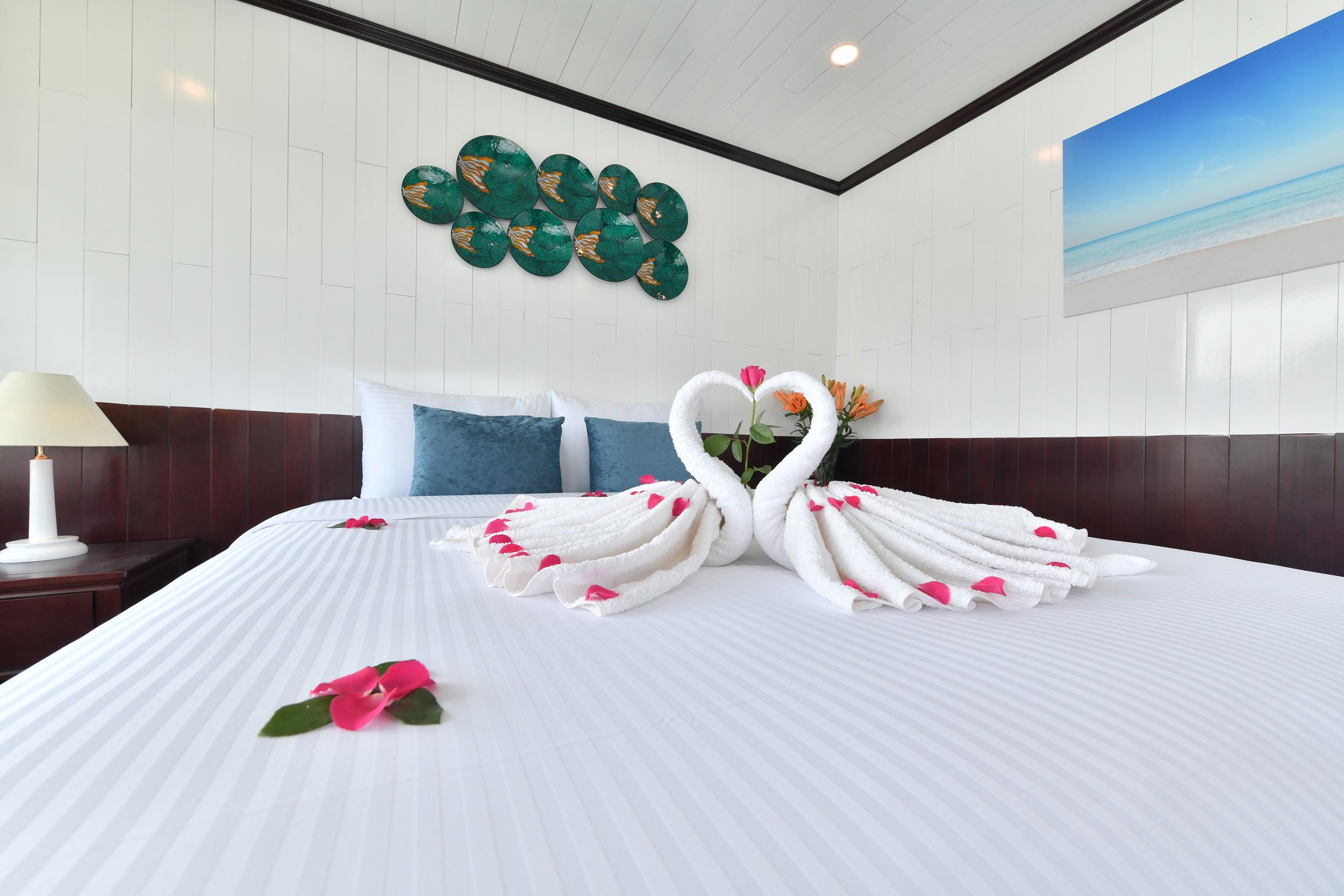 A hotel room with a neatly made bed, a decorative wall piece, and a painting of a beach scene.