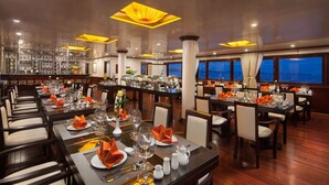A well-lit dining area with multiple tables set for service, featuring a bar area in the background. - Halong Sapphire Cruise (Tuan Chau)