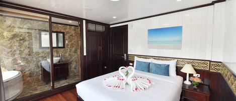 A hotel room with a large bed, a bathroom with a stone wall, and a view of the sea.