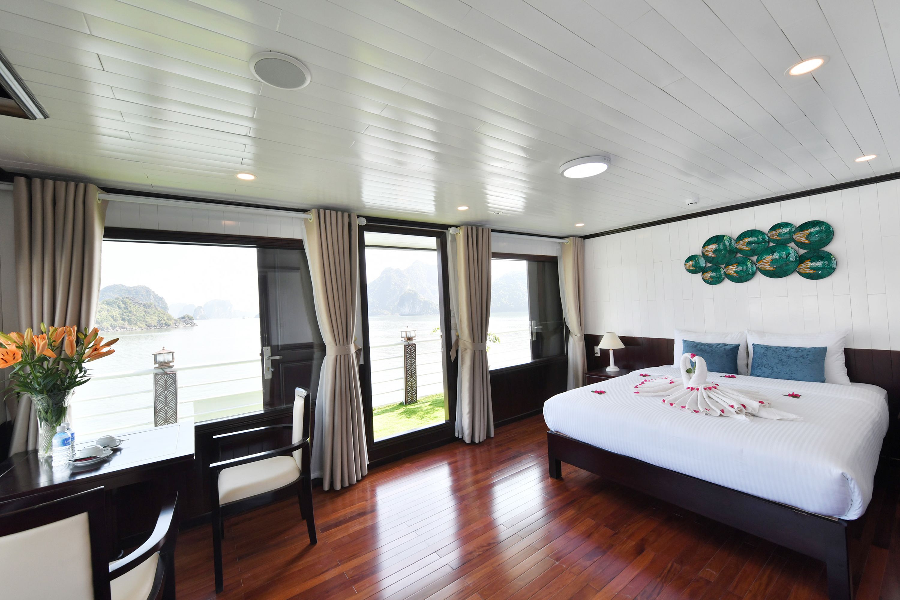 Une chambre d’hôtel avec un grand lit, un bureau avec des chaises, une vue sur la mer et un mur décoré de motifs circulaires.