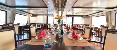 A dining area with tables set for two, featuring a central vase with flowers, clear glasses, and neatly folded napkins.