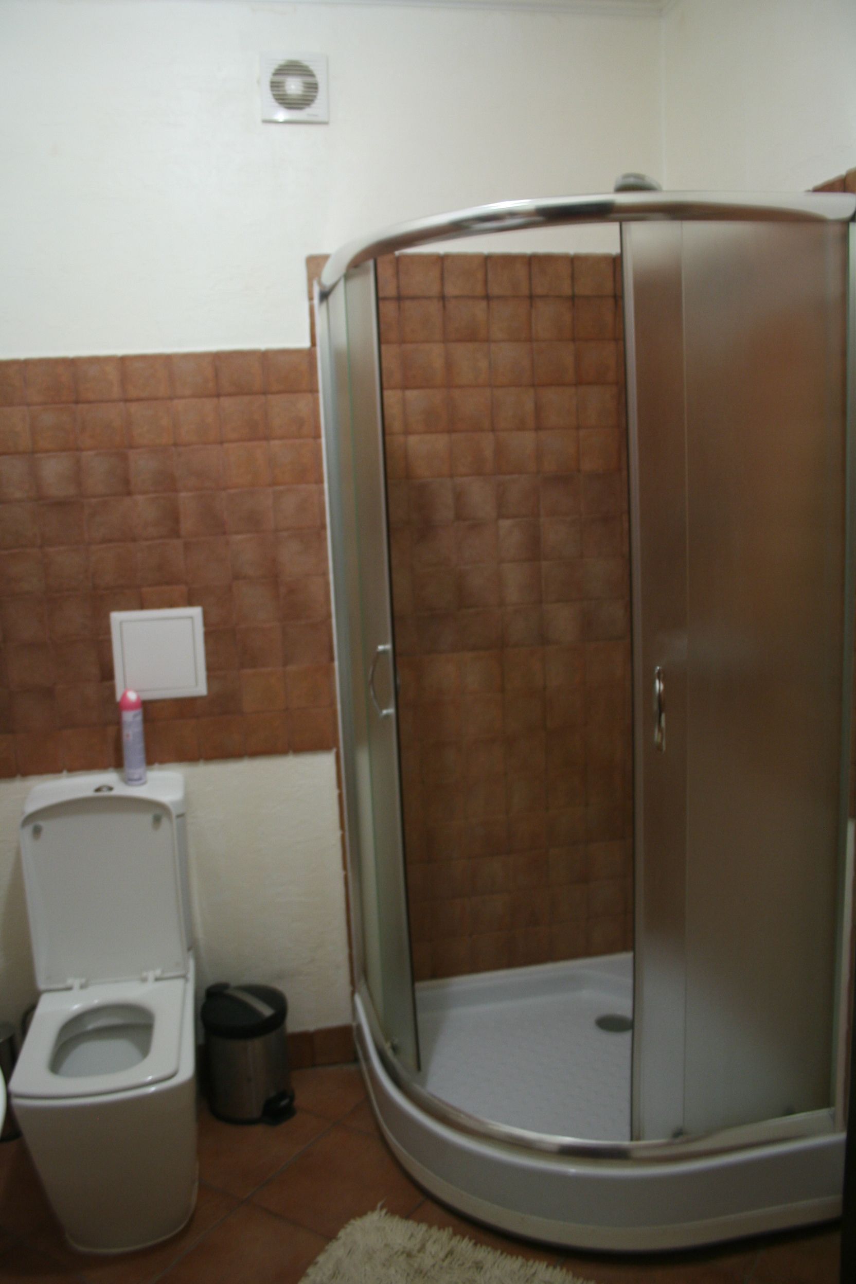 A bathroom with a toilet, a trash bin, and a shower enclosure.