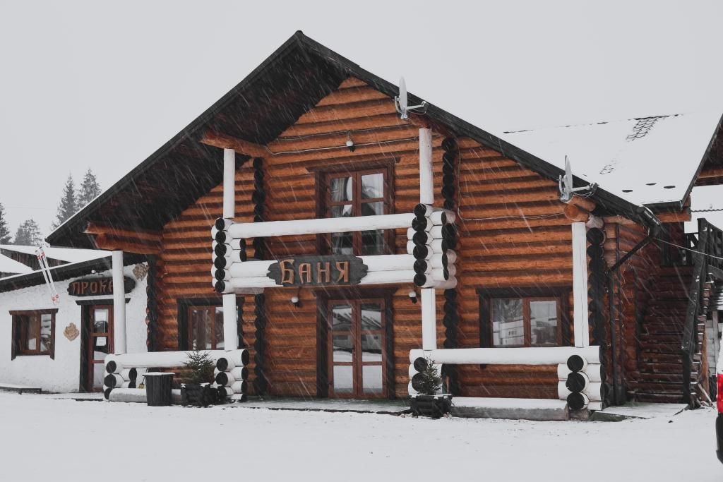 A log cabin with a sign reading "БАНЬ" and a snow-covered exterior.