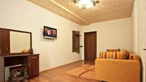 A room with a wooden floor, a sofa, a television, a wooden cabinet, and a door. - Hotel Shulc (Bukovel)
