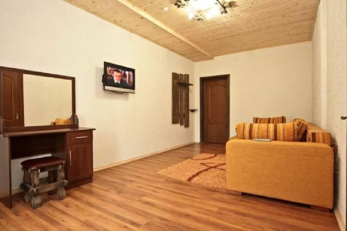 A room with a wooden floor, a sofa, a television, a wooden cabinet, and a door.