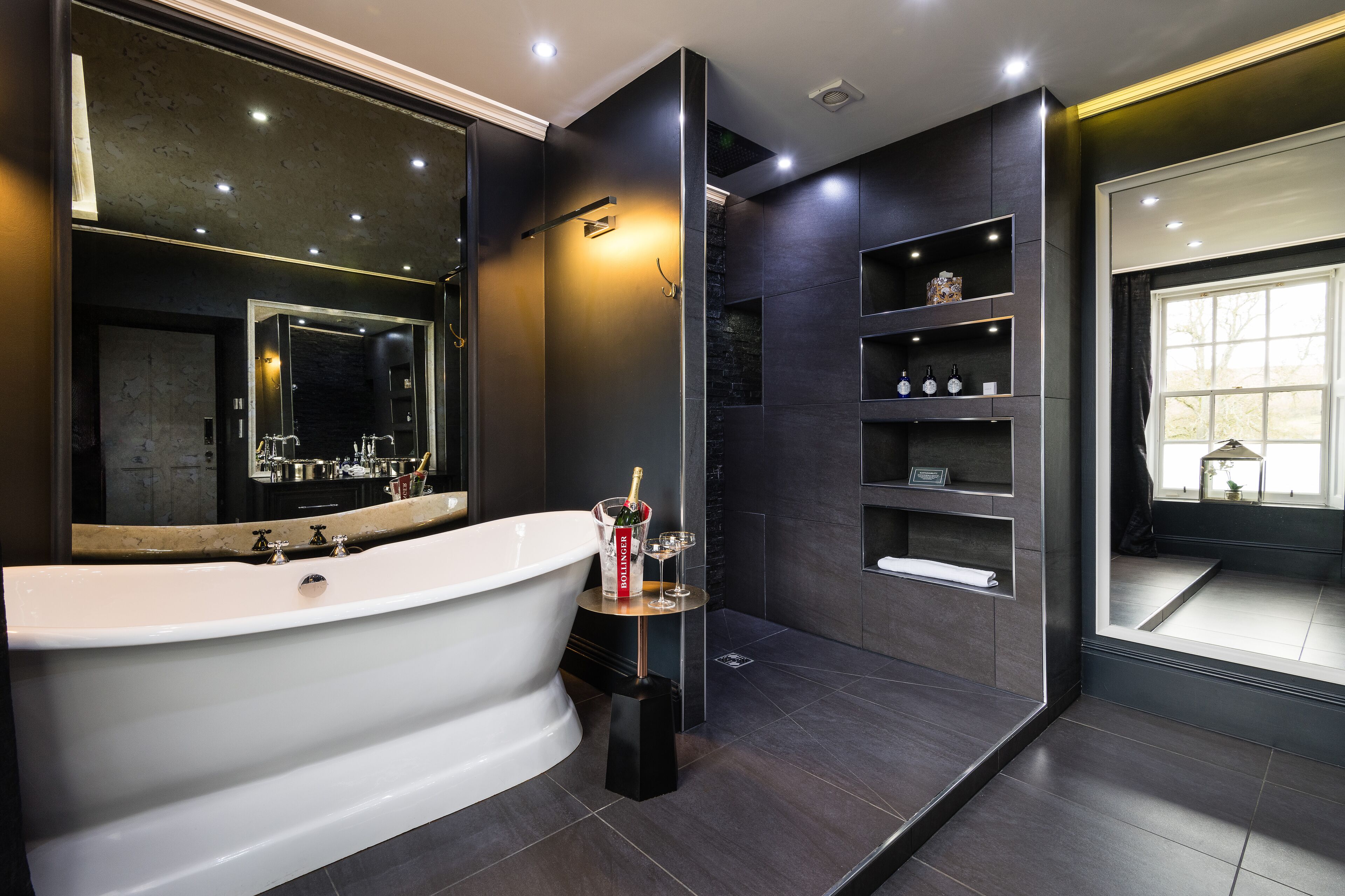 Un baño moderno con una bañera independiente, un espejo grande y estantes integrados.
