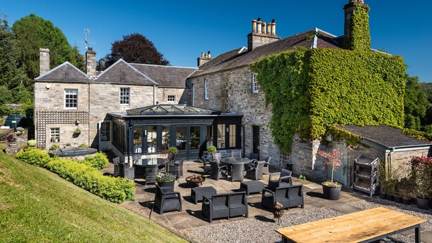 A stone building with ivy-covered walls, outdoor seating, and a glass-roofed structure. - The Old Manse of Blair (Pitlochry)