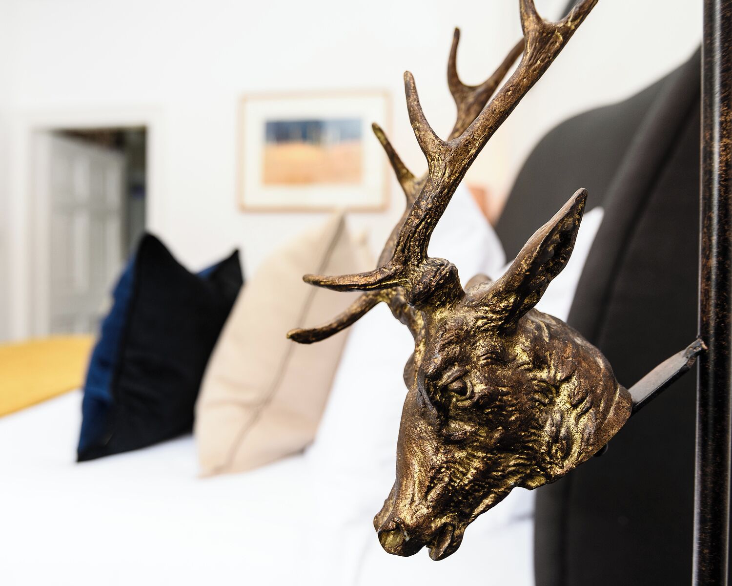 A room with a bed, a framed picture on the wall, and a mounted deer head on the wall.