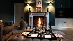 A cozy living room with a fireplace, a dining table set for two, and a comfortable sofa. - The Old Manse of Blair (Pitlochry)