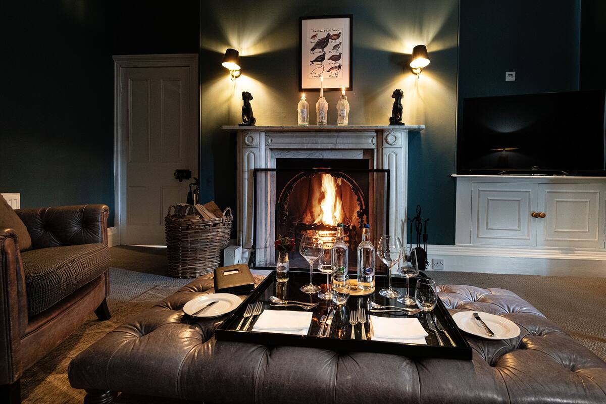 A cozy living room with a fireplace, a dining table set for two, and a comfortable sofa.
