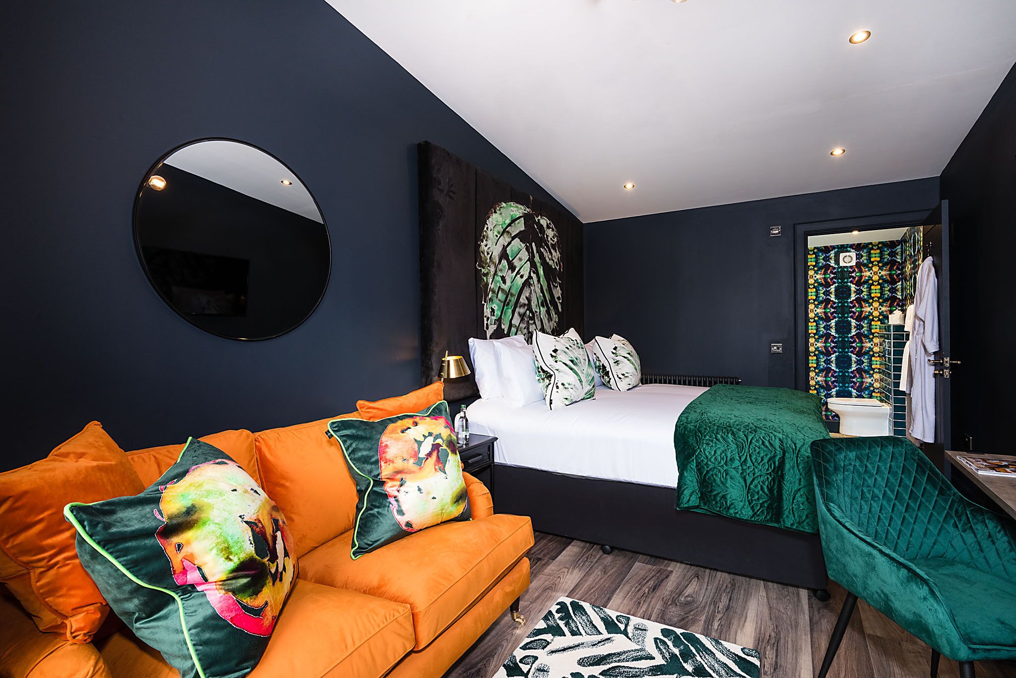 Ein modernes Schlafzimmer mit einem Bett, einem runden Spiegel, einem orangefarbenen Sofa und einem grünen Sessel.