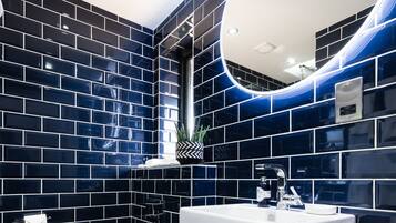 Une salle de bain moderne avec des murs recouverts de carreaux noirs, un lavabo blanc et des toilettes.