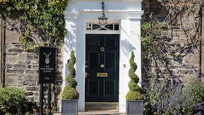 A black door with a brass knocker, flanked by two potted topiaries, and a sign reading "The Old Manse of Blair." - The Old Manse of Blair (Pitlochry)