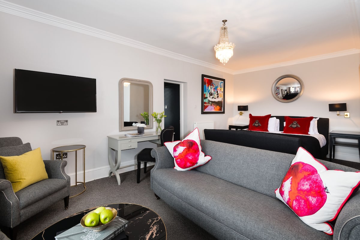 A modern living room with a grey sofa, a flat-screen TV, a desk, and a chandelier.