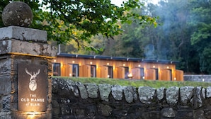 A stone wall with a sign reading "The Old Manse of Blair" and a modern building in the background. - The Old Manse of Blair (Pitlochry)