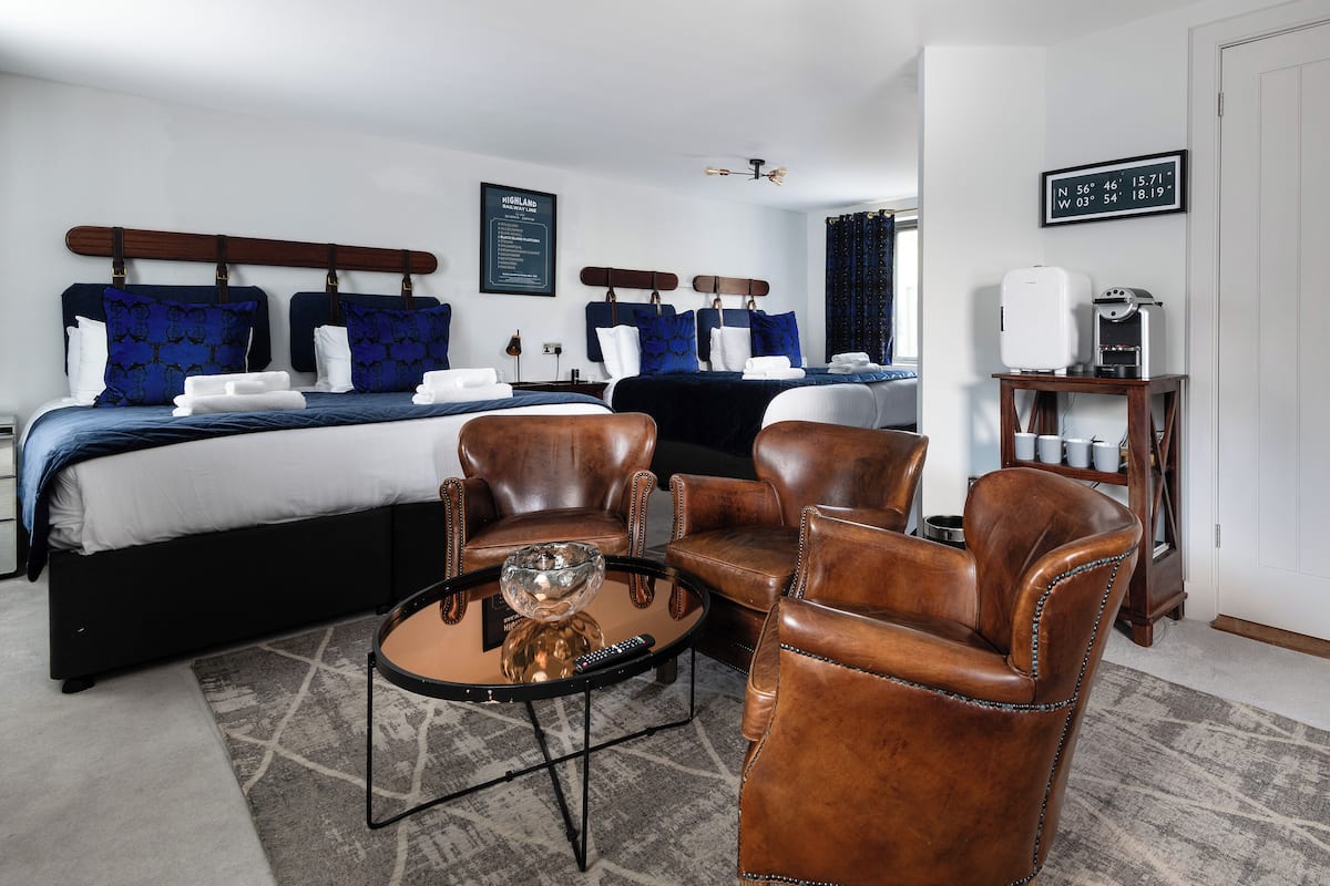 A hotel room with a large bed, two armchairs, a coffee machine, and a small table with a glass bowl.