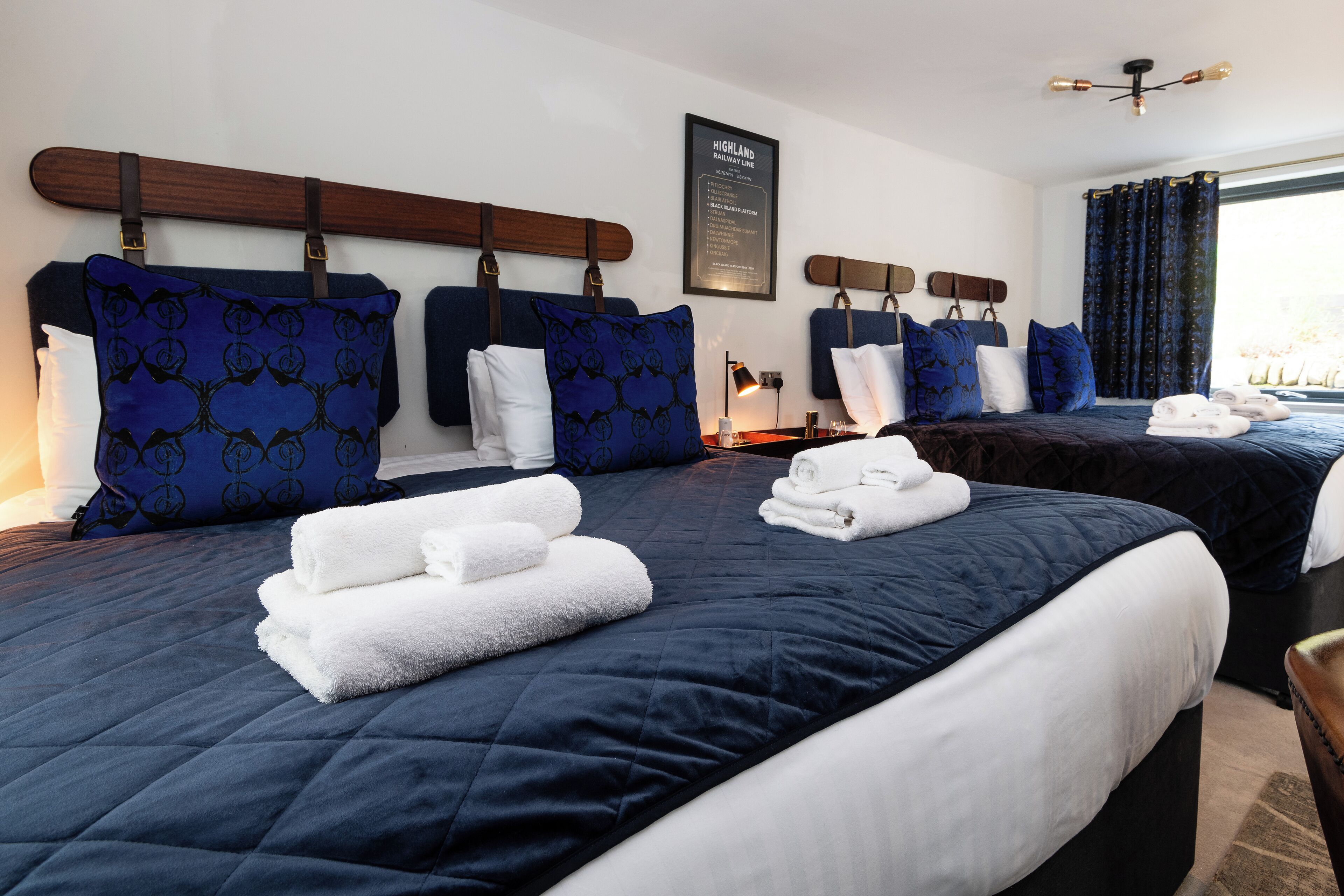 A hotel room with two beds, each with a dark blue bedspread and matching pillows. There are white towels neatly folded on each bed.