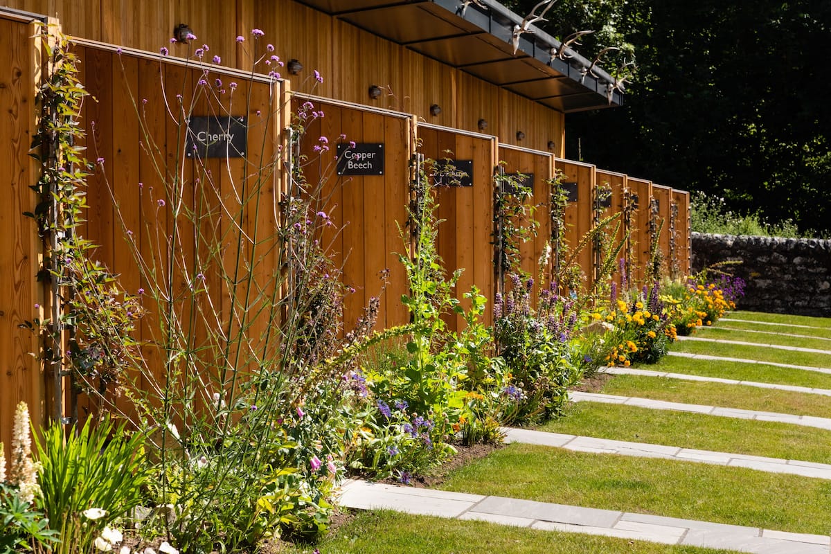 A wooden fence with signs indicating different garden sections.