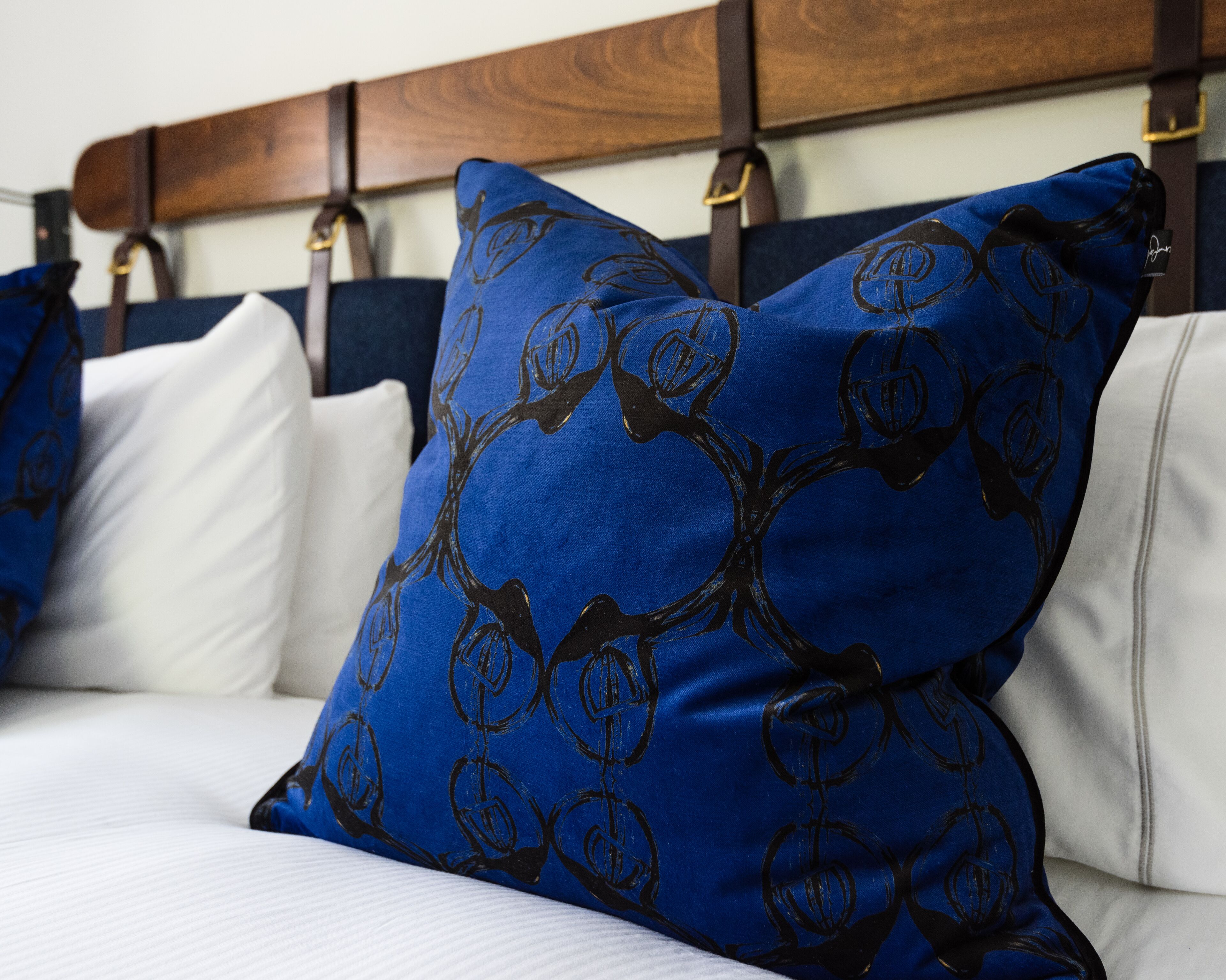 Un lit avec une literie blanche et des oreillers bleus ornés d’un motif noir.