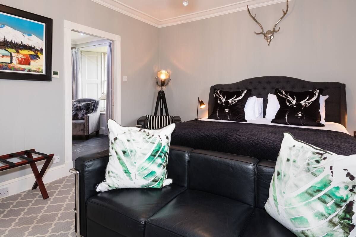 A modern bedroom with a large bed, a black leather sofa, and a mounted deer head.