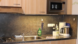 A kitchen with a stainless steel sink, a microwave, a kettle, and a coffee maker. - Ferienapartmenthaus Hubertushof (Mittenwald)