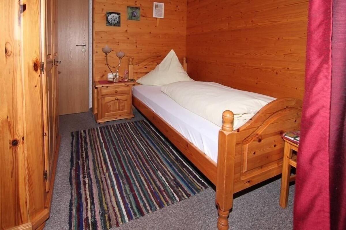 A wooden room with a bed, a nightstand, a door, and a wall with pictures.