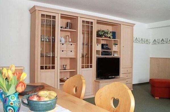 A dining area with a wooden table, chairs, and a cabinet with glass doors. - Ferienapartmenthaus Hubertushof (Mittenwald)