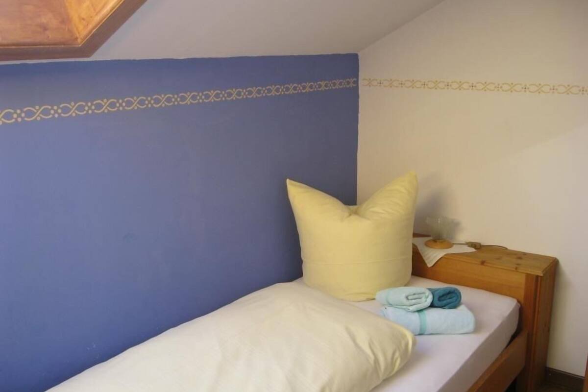 A single bed with a wooden headboard, a blue wall, and a patterned border.
