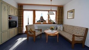 A cozy living room with a sofa, two armchairs, a small table, a television, and a window with curtains. - Ferienapartmenthaus Hubertushof (Mittenwald)